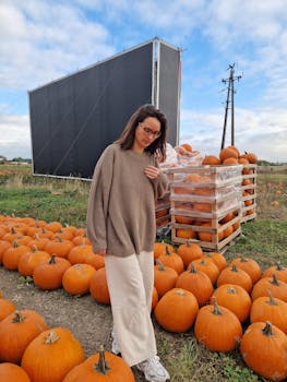 穿着舒适毛衣的女人站在户外，周围是秋天的南瓜