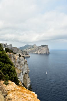 在多云的天空下，俯瞰着宁静的蓝色大海，绿树成荫的雄伟沿海悬崖显得格外雄伟
