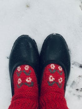 Black shoes with red floral socks on snowy ground, overhead view.