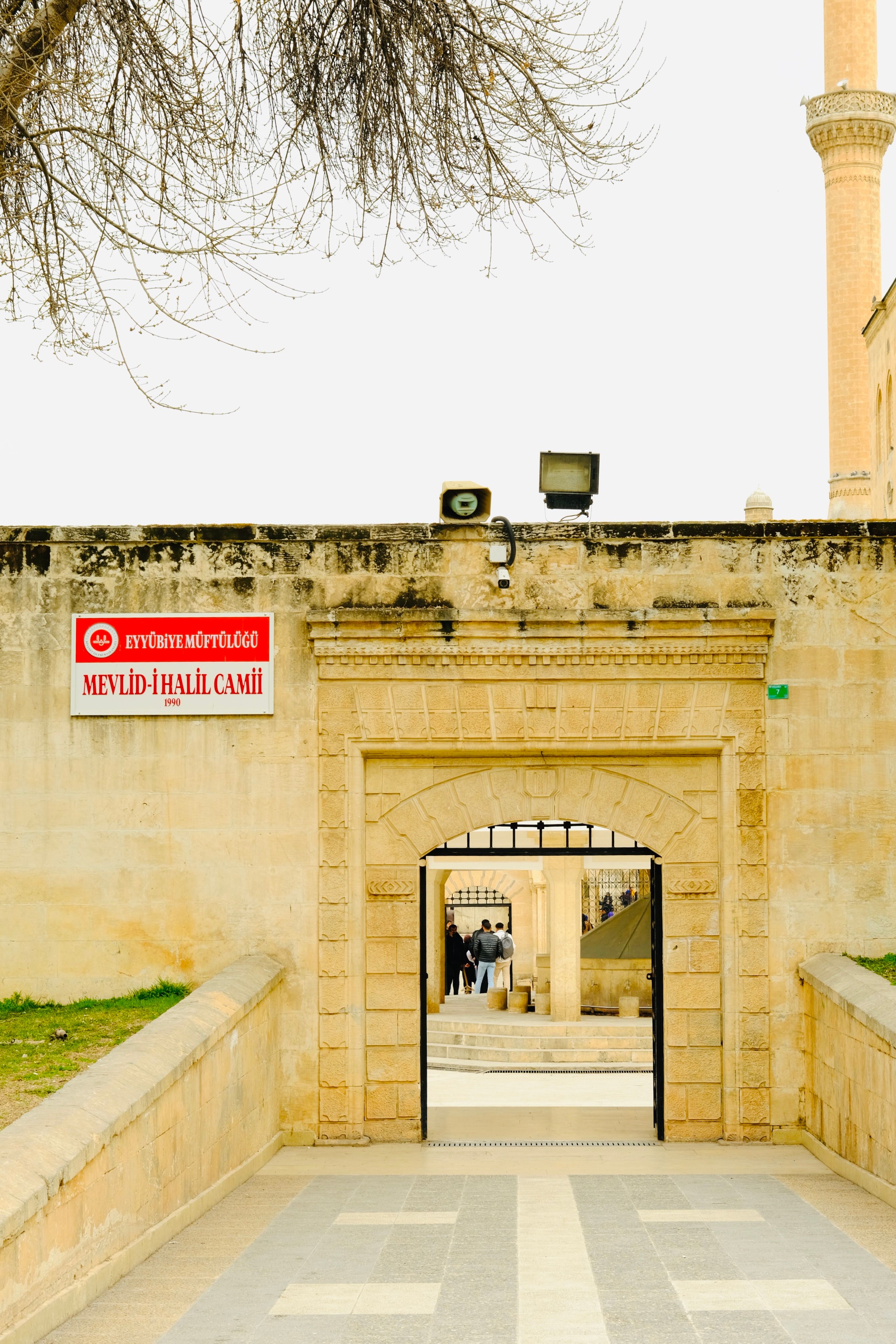 Entrance to Mevlid-i Halil Mosque with winter foliage and sandstone architecture.