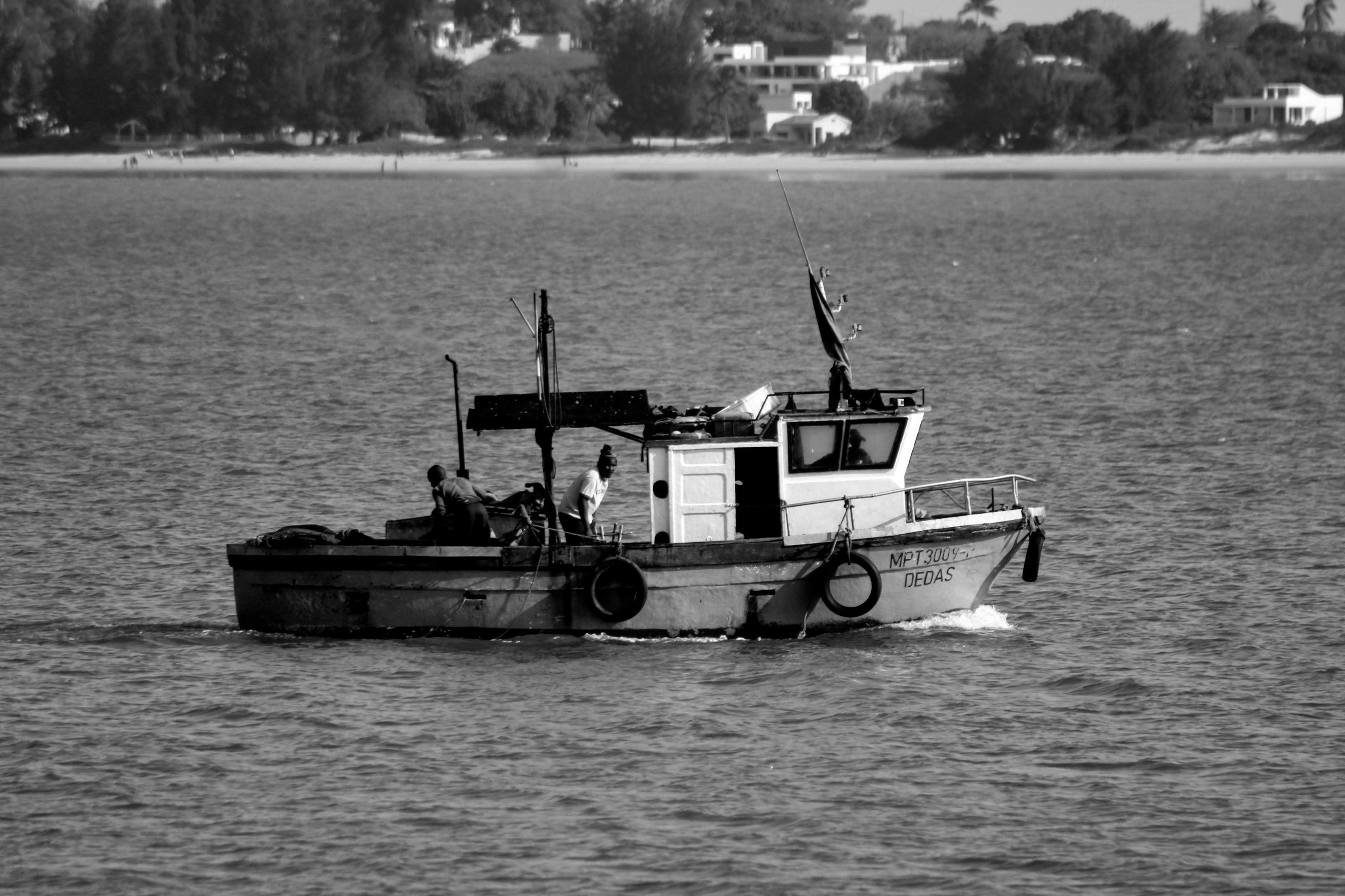在靠近海岸的宁静大海上，一艘渔船和船员构成了一幅黑白照片