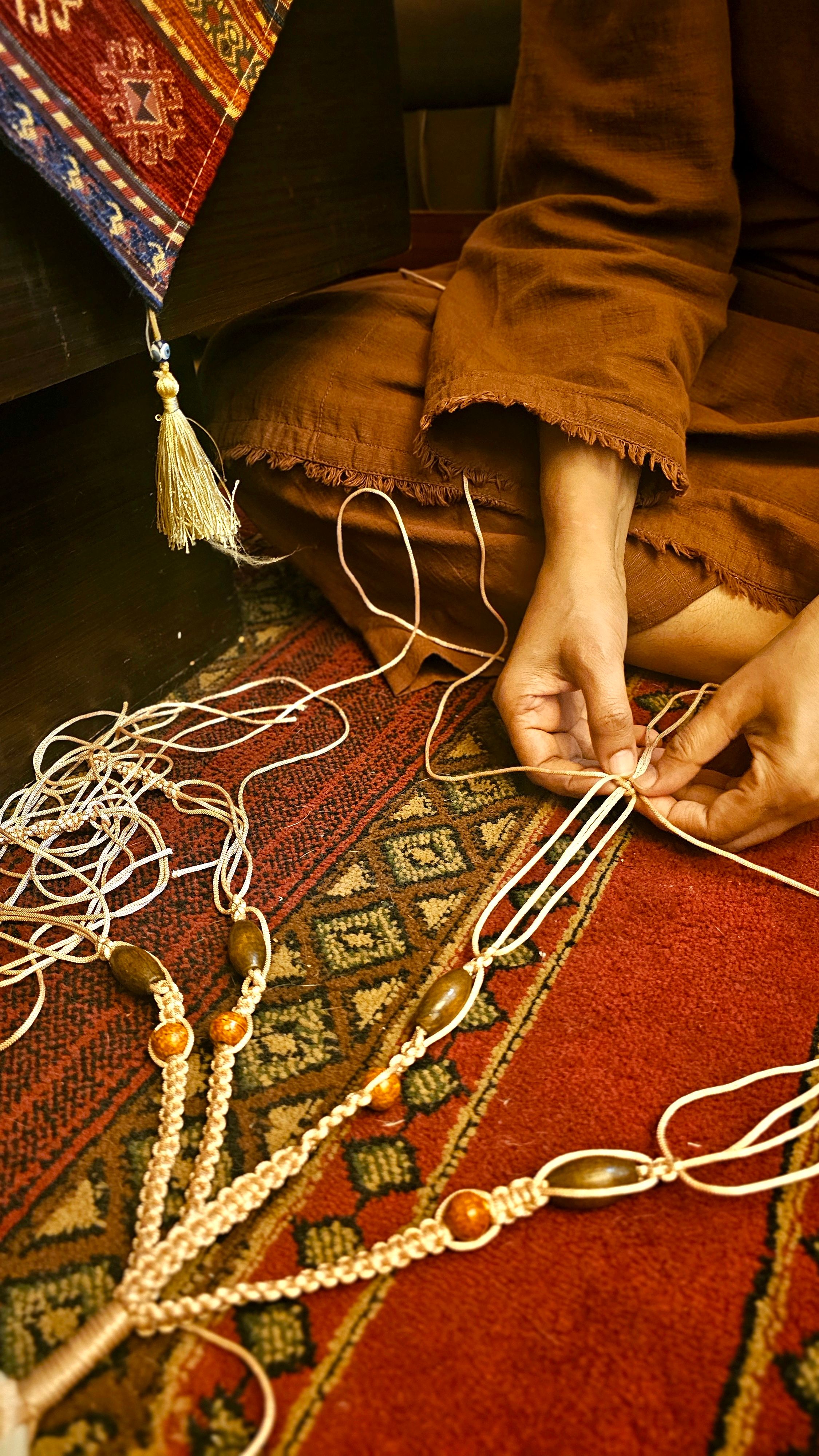 A person skillfully weaving on a patterned carpet with intricate thread designs and beads.