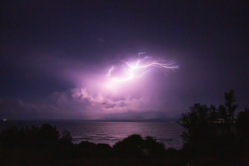 Free Capture of a powerful lightning bolt illuminating the night sky over a calm ocean, creating a dramatic and moody atmosphere. Stock Photo