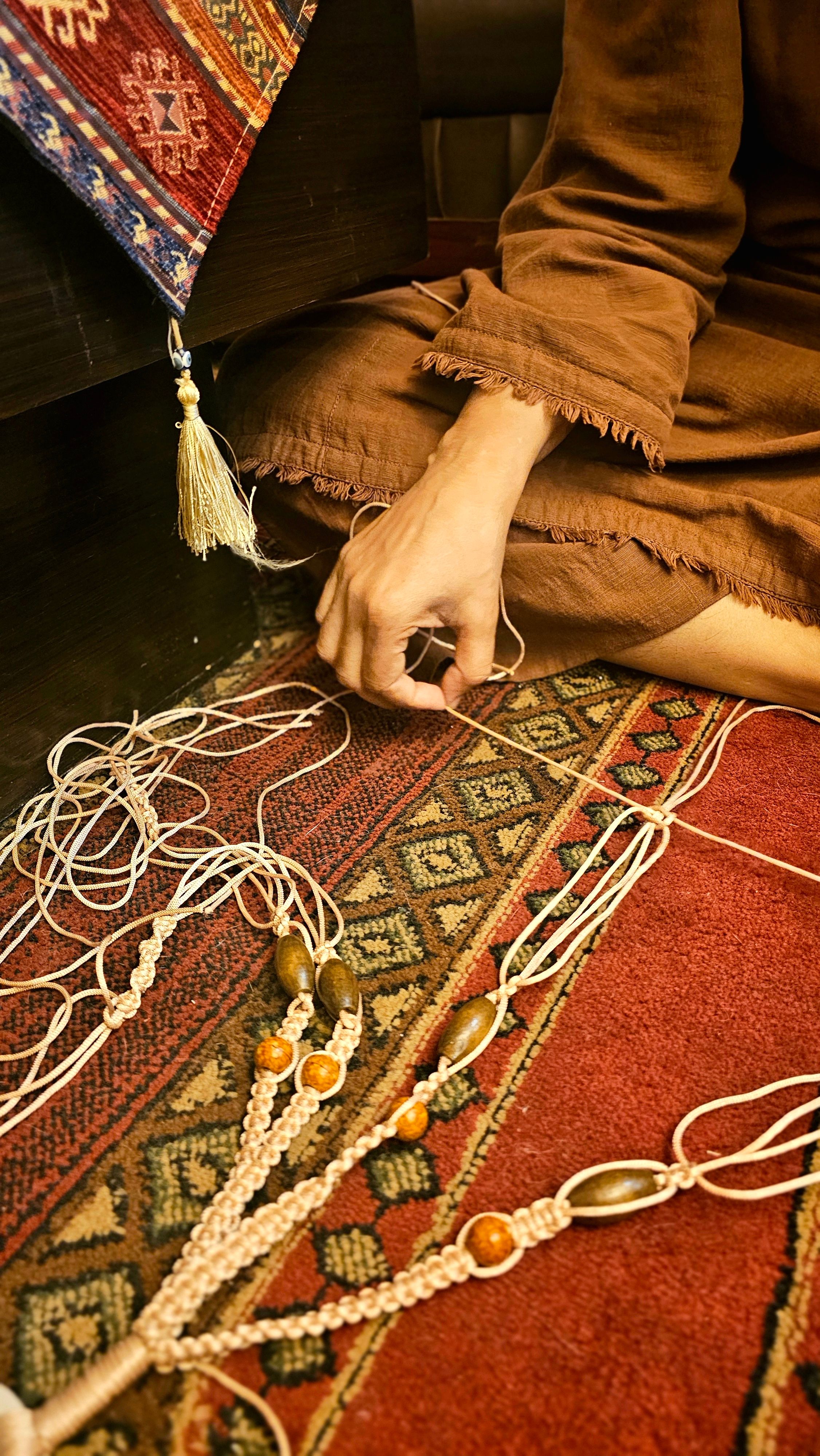Close-up of an artisan creating traditional tassel waistbands on a patterned rug.