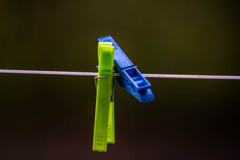 Bright green and blue clothespins clipped on a clothesline against an outdoor backdrop.