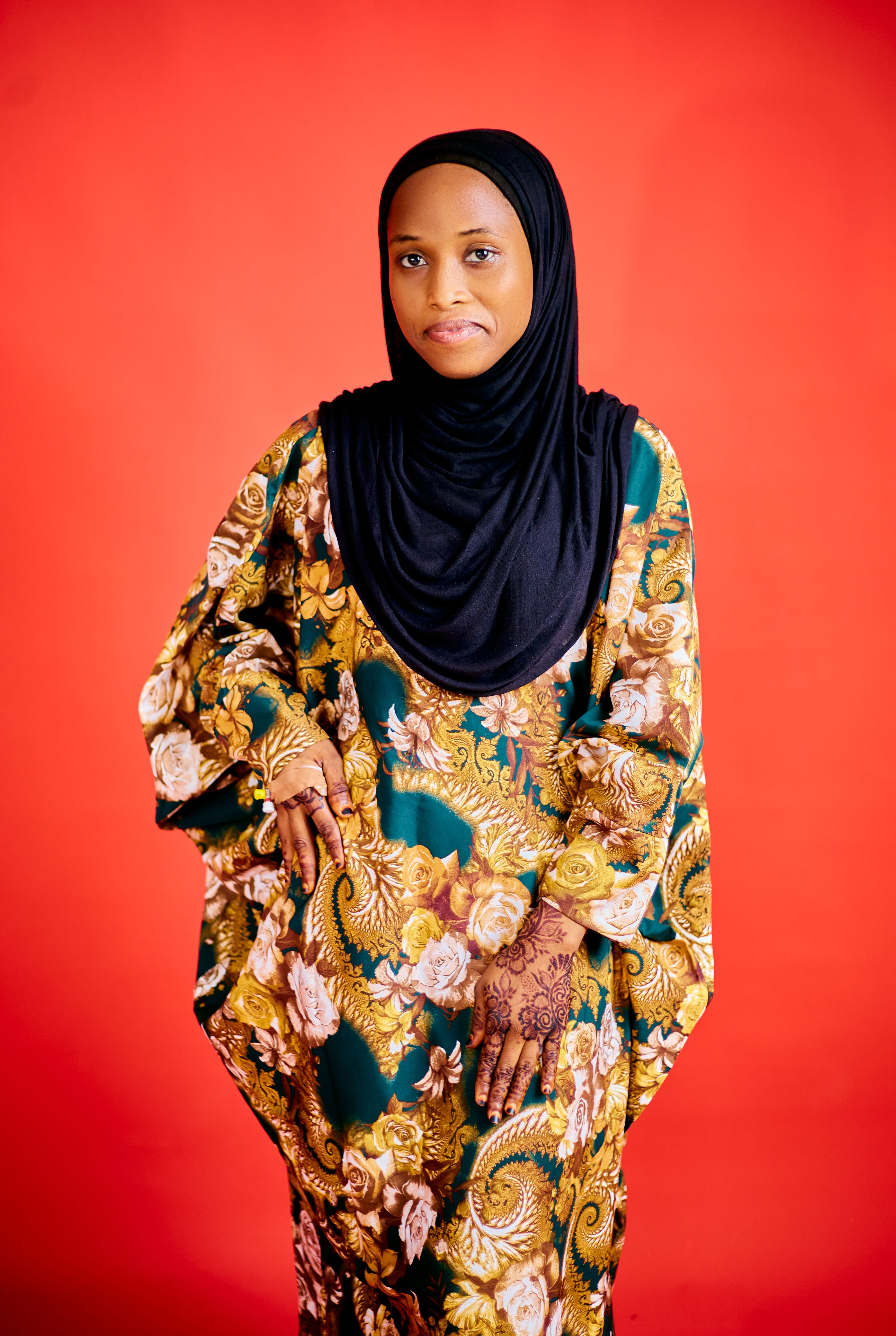 Portrait of a woman in a floral traditional dress and hijab on a red background.