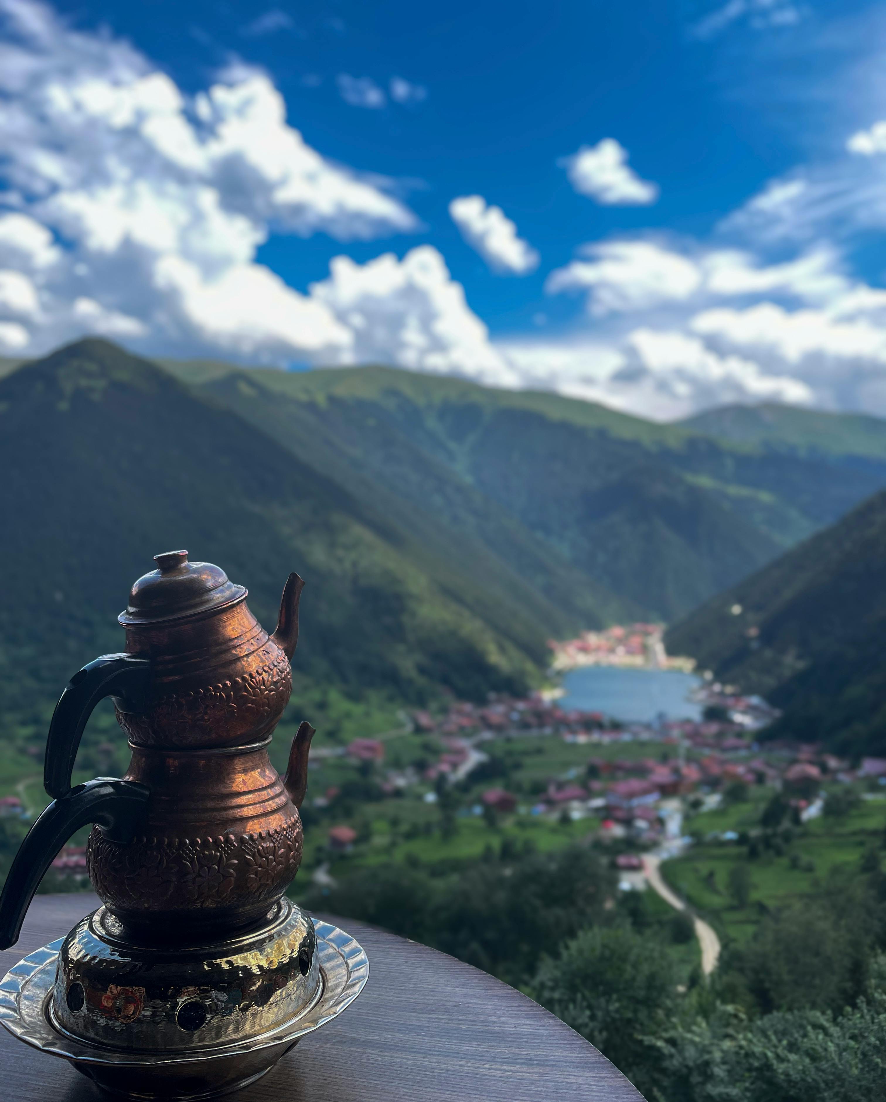 桌子上摆放着装饰茶壶，从高处俯瞰时可以看到风景如画的山间湖泊和村庄
