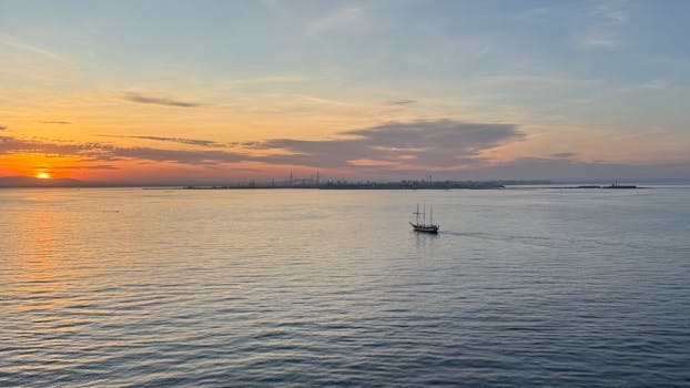 加的斯湾上空，宁静的日落映照着平静的水面，一艘孤独的帆船静静地漂浮着