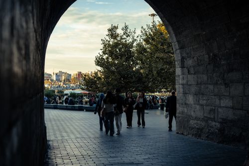 Free People walking through a stone archway with a cityscape backdrop at sunset. Stock Photo