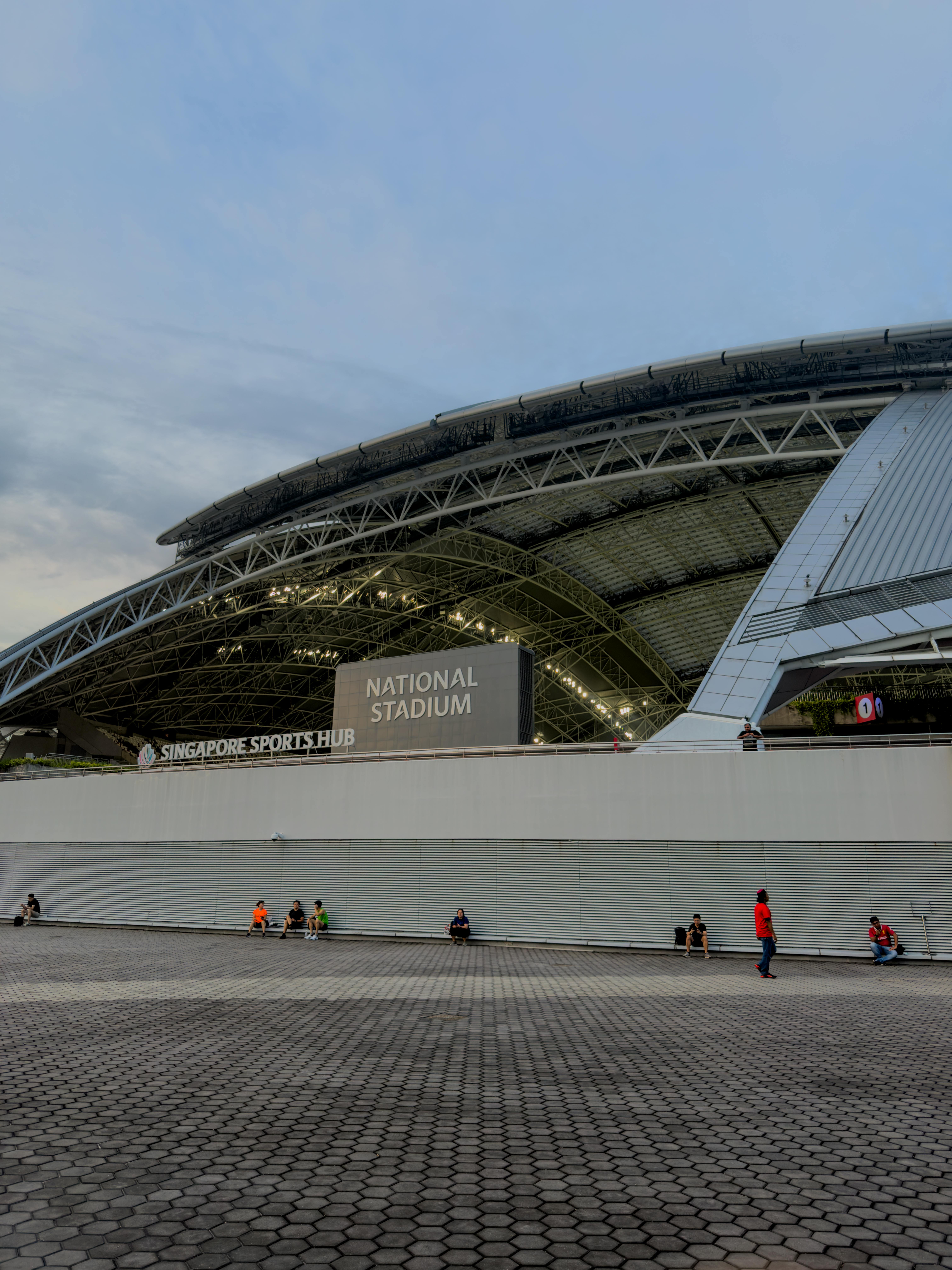 黄昏时，新加坡国家体育场的外部视野广阔，前景中几个人正在拍摄