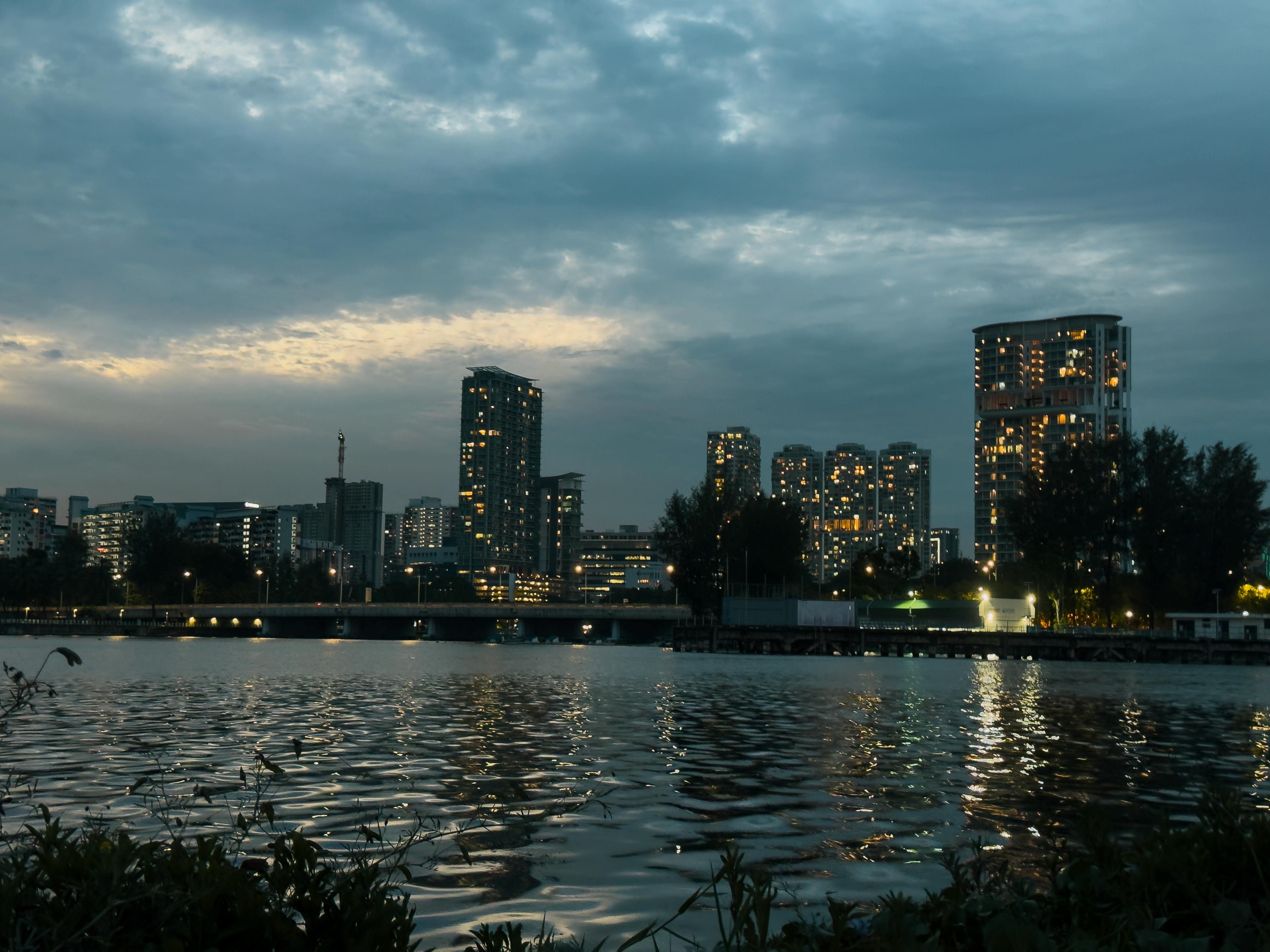 黄昏时，城市天际线在多云的天空下，反射着平静水面上的灯光