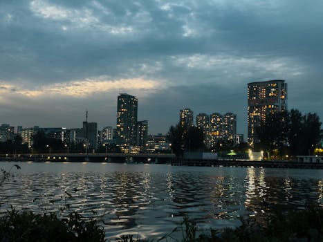 黄昏时，城市天际线在多云的天空下，反射着平静水面上的灯光