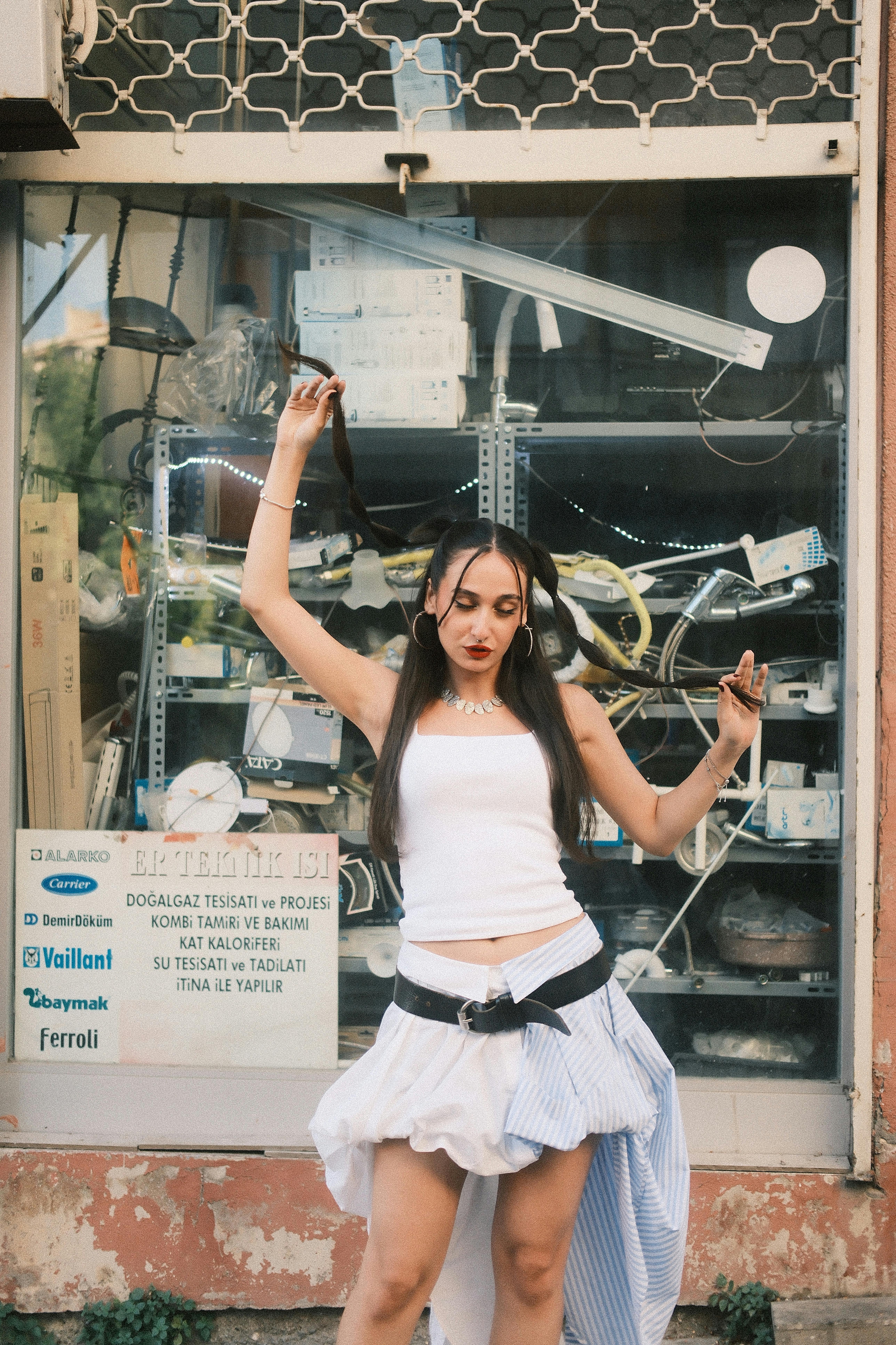 A young woman in casual attire poses playfully outside a store window.