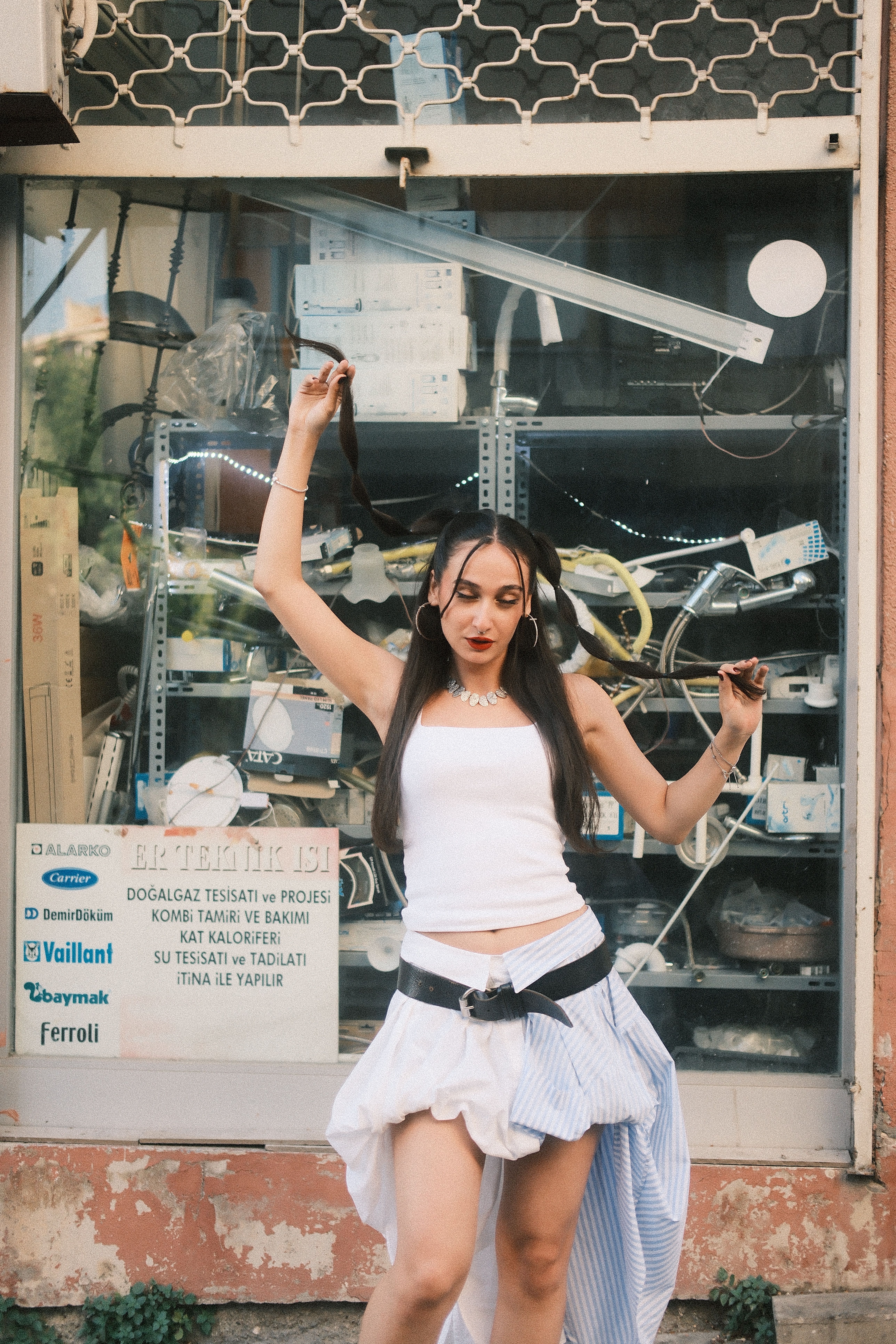 Woman in white top and skirt poses confidently in front of a shop display.