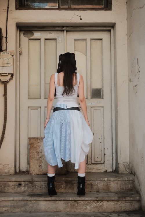 Free Back view of a woman in a creative skirt standing before a weathered building door. Stock Photo