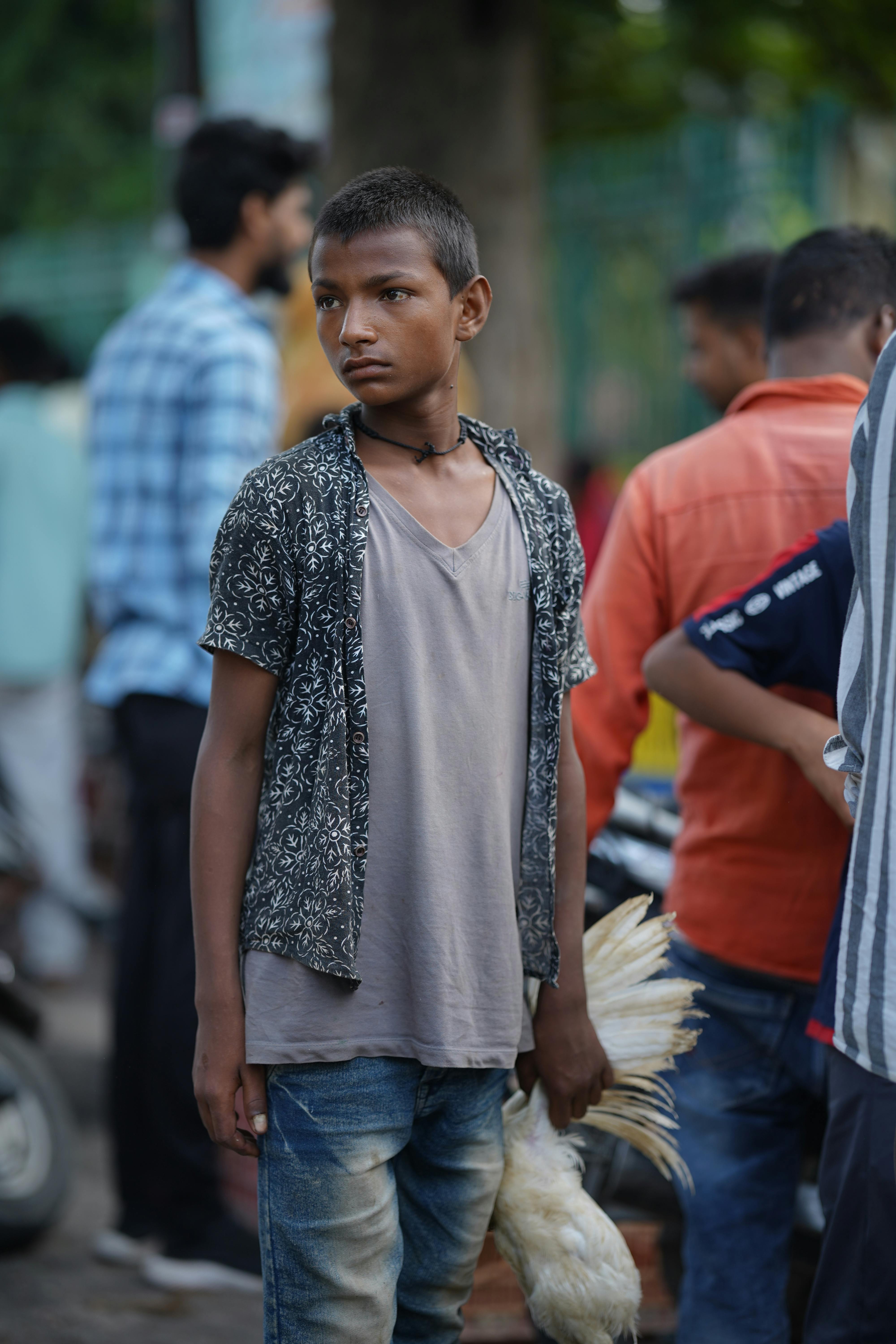 Young boy holding chicken in bustling outdoor market setting.