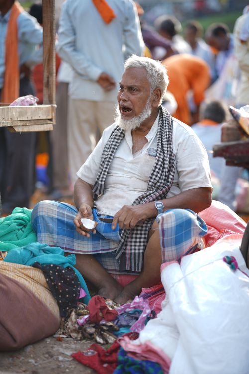 Free Elderly man with a white beard selling goods at a colorful outdoor market. Stock Photo