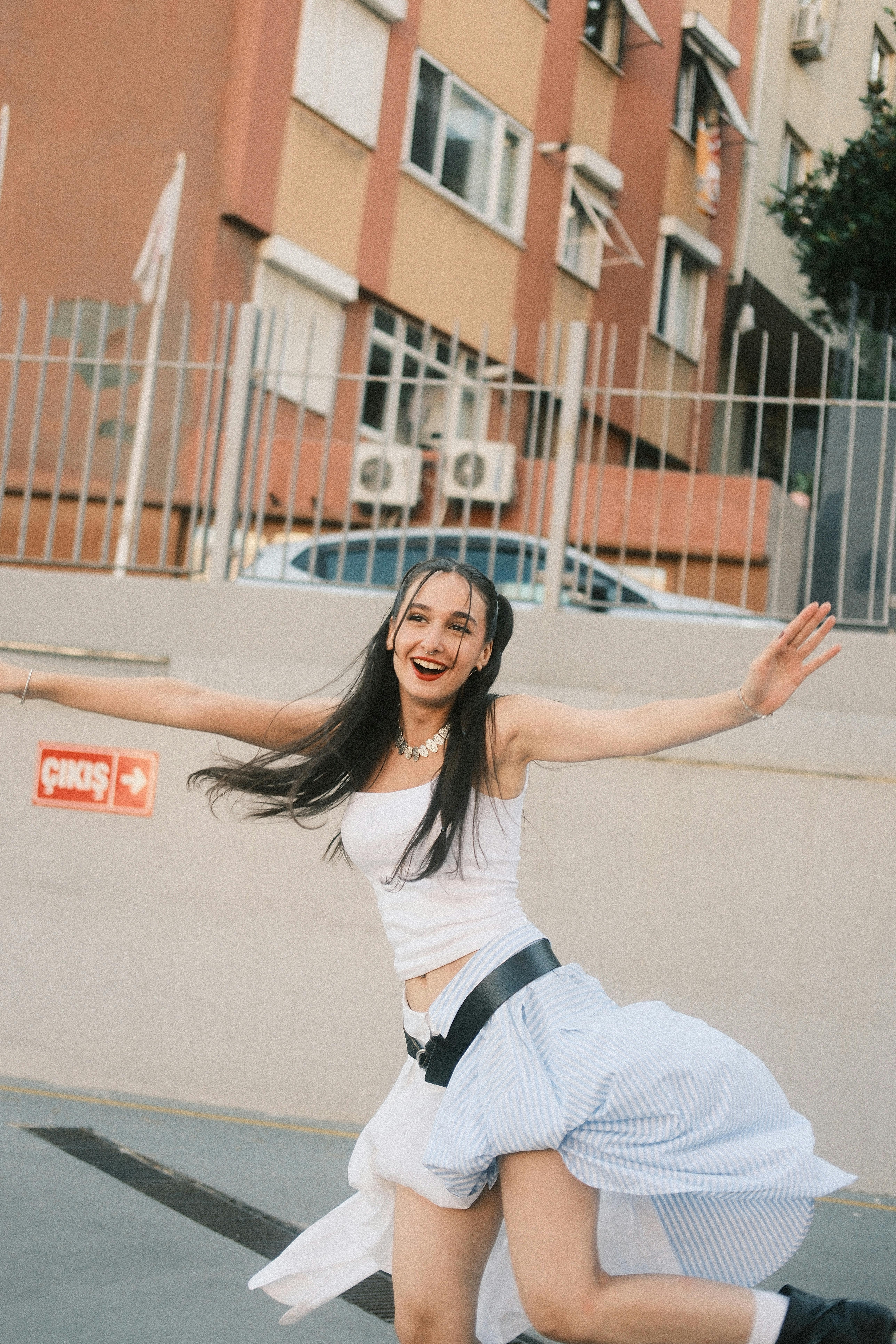 Happy young woman with flowing hair dancing joyfully outside on a sunny day by urban buildings.
