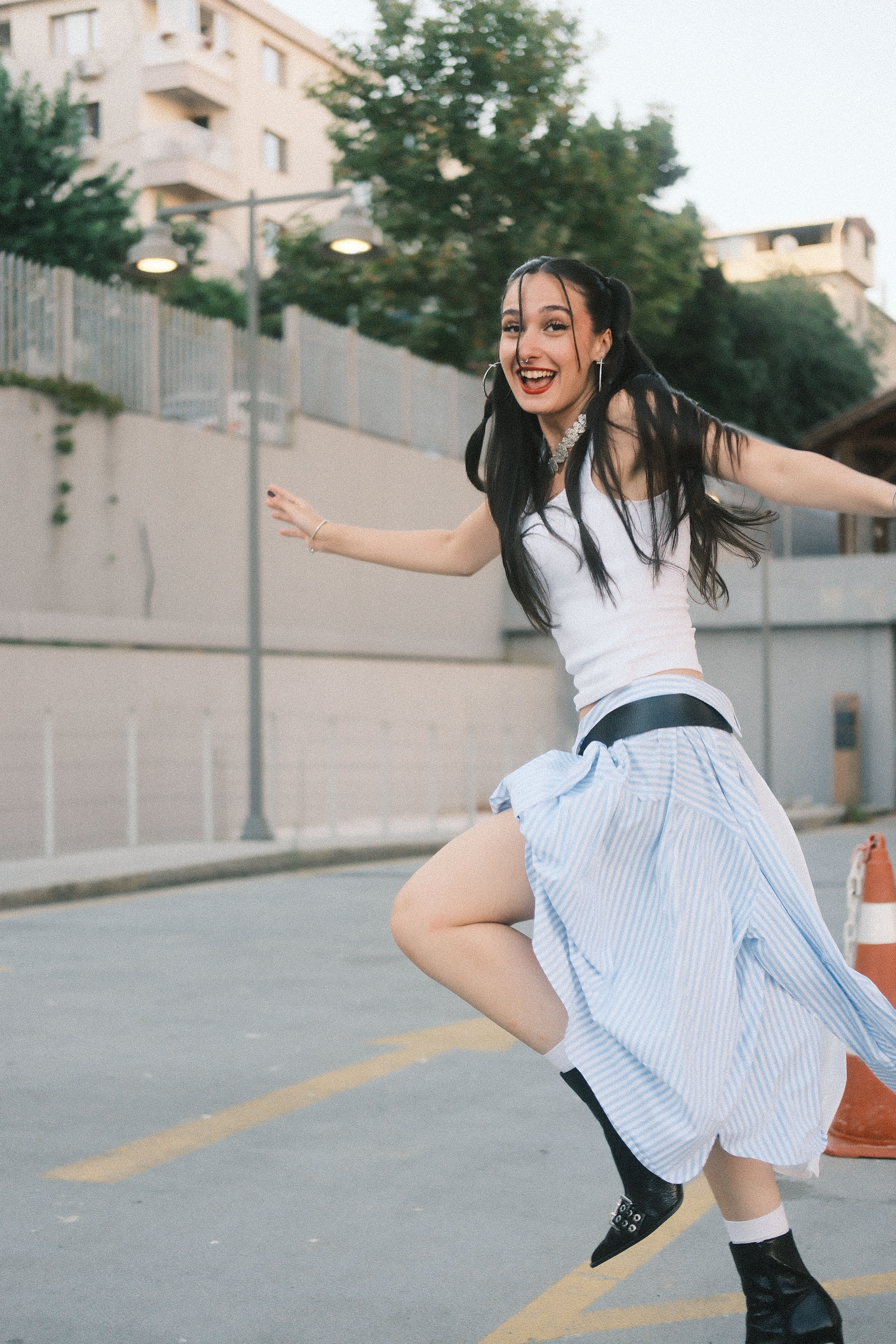 Energetic young woman in a street, expressing joy with a playful dance in a casual skirt. Urban vibe.