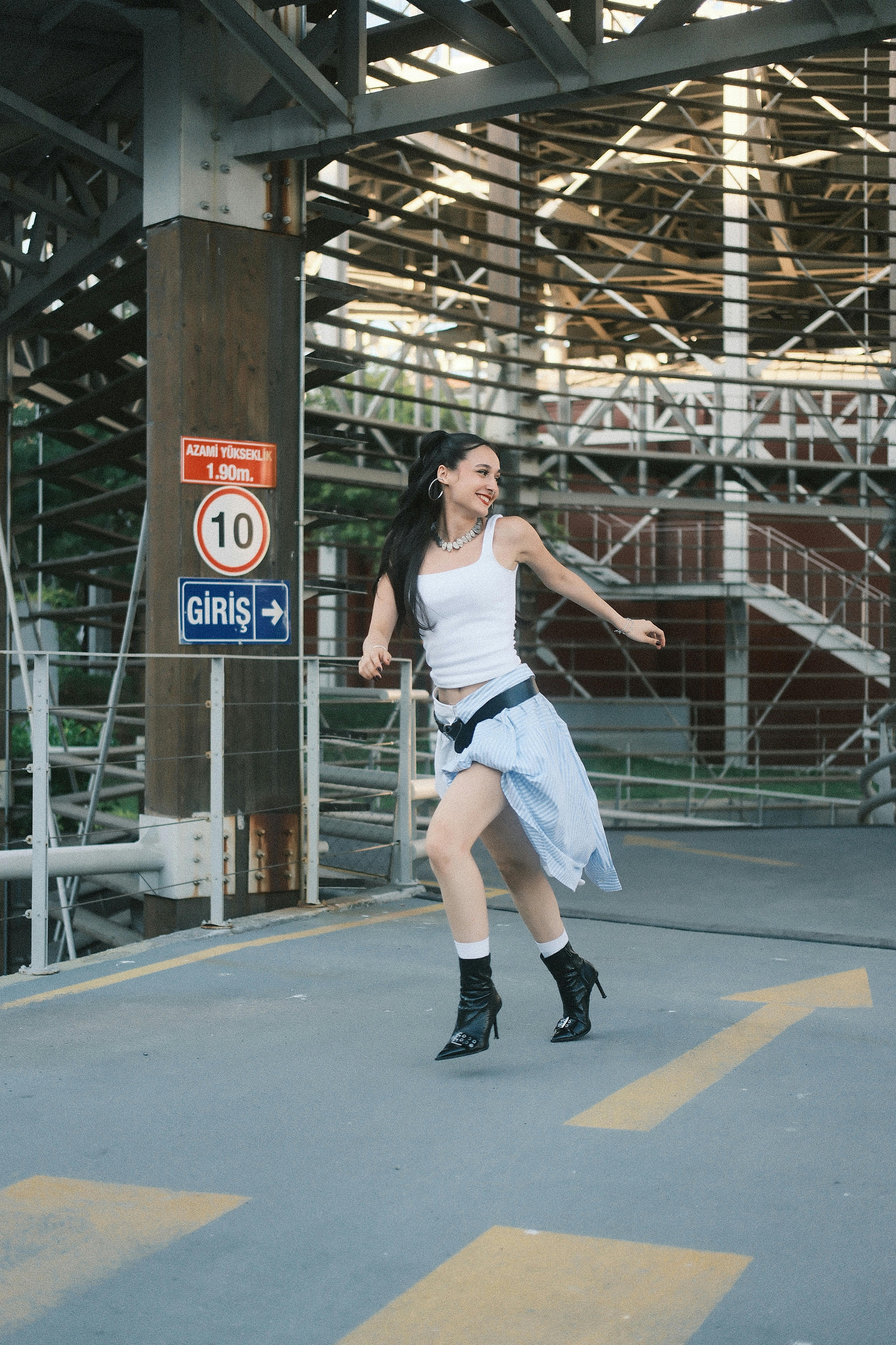 A cheerful young woman dancing on an urban street with stairs in the background.