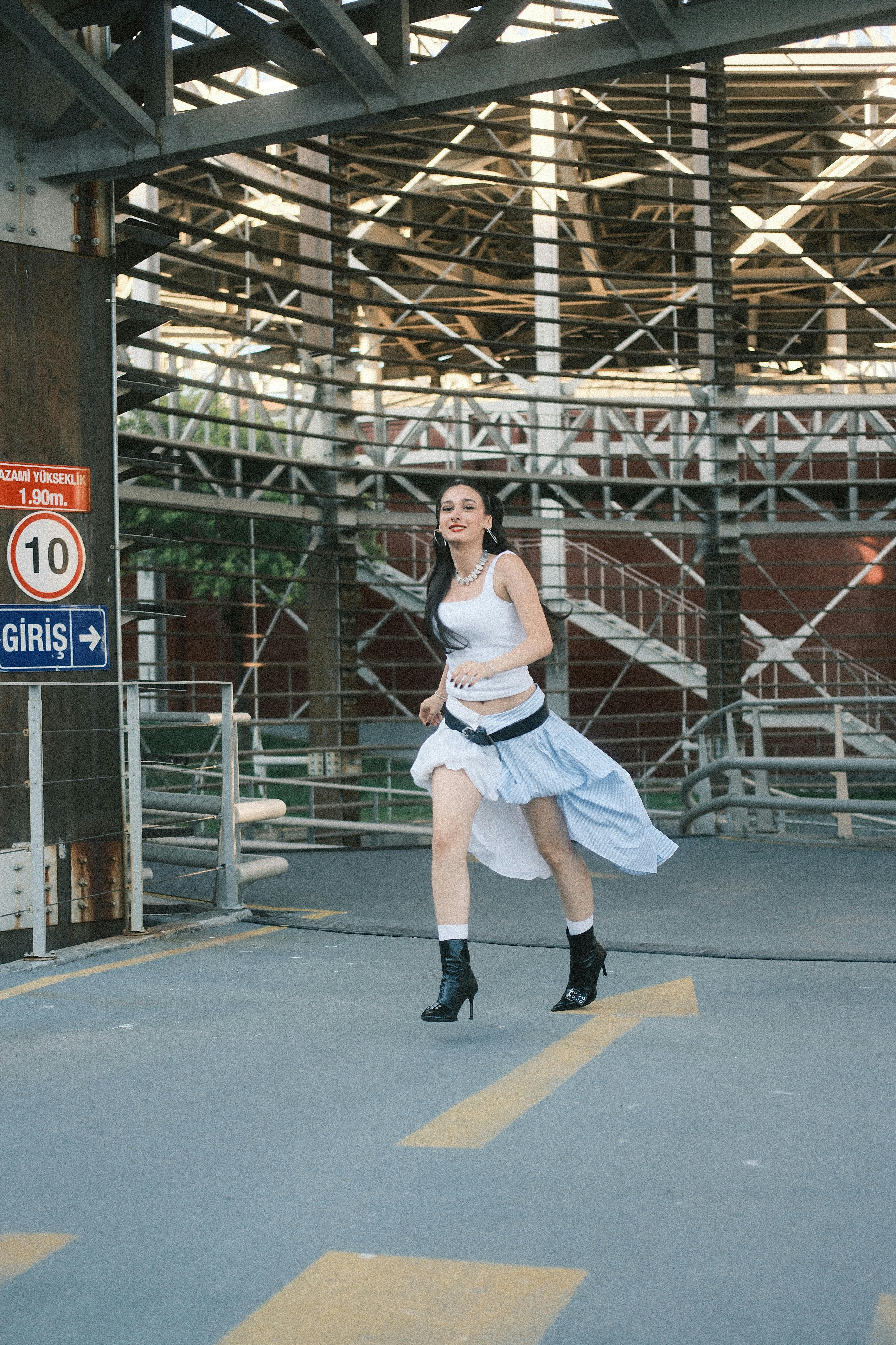 A young adult woman in a white top runs joyfully beneath an urban overpass, embodying freedom and movement.
