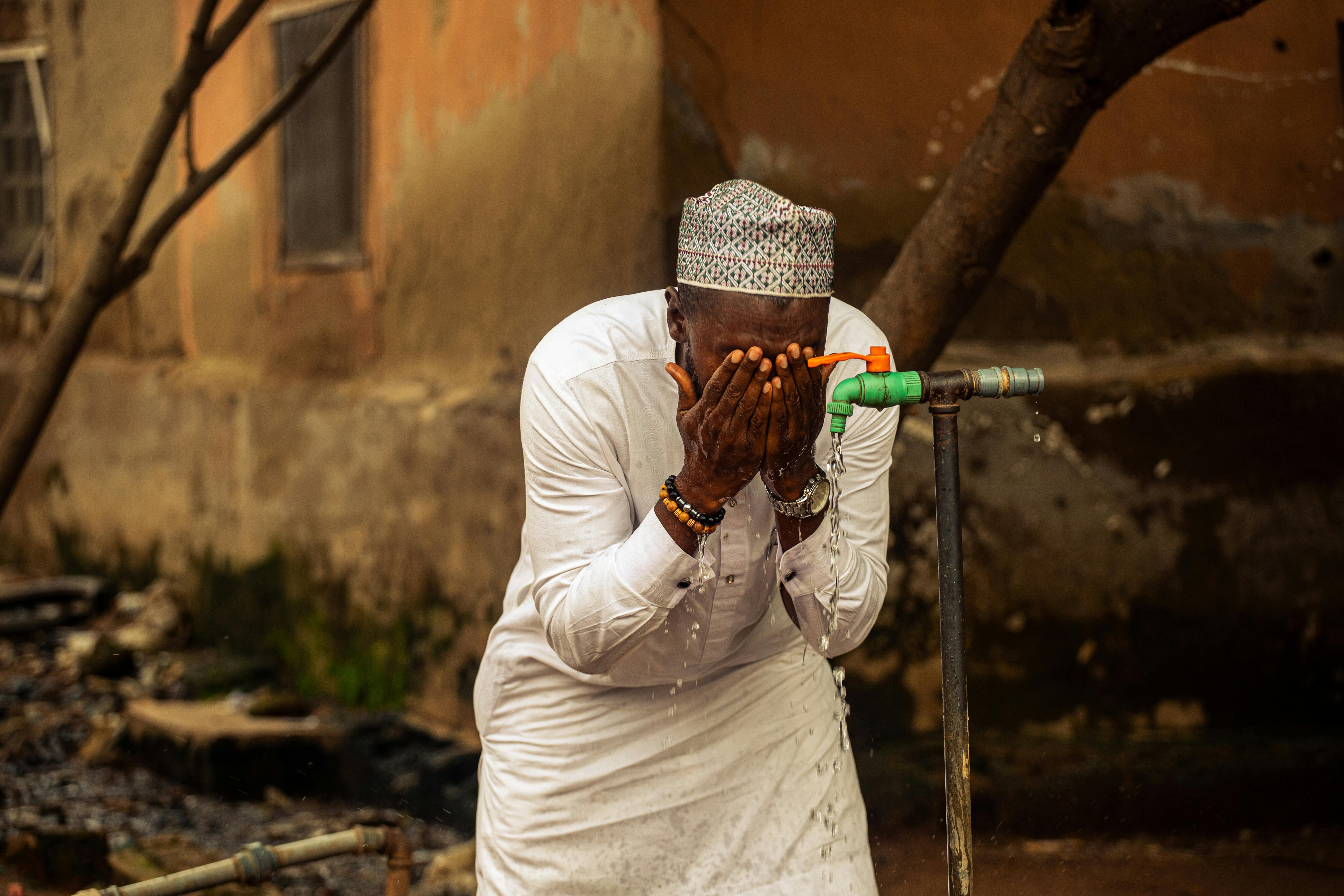 An adult man washing his face at an outdoor tap, showcasing daily life in Nigeria.