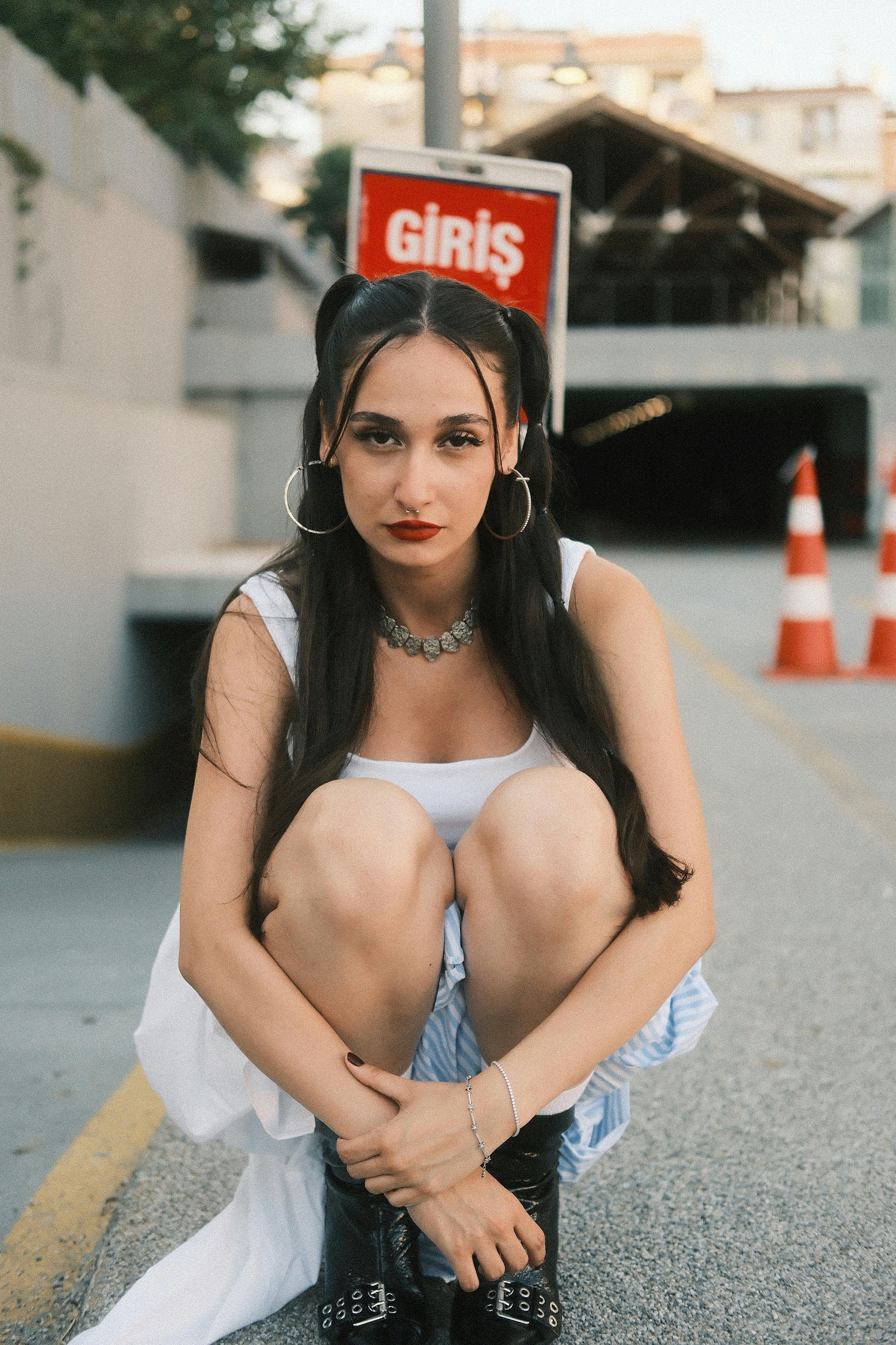 Urban portrait of a young woman squatting by an entrance with a 'Giriş' sign.