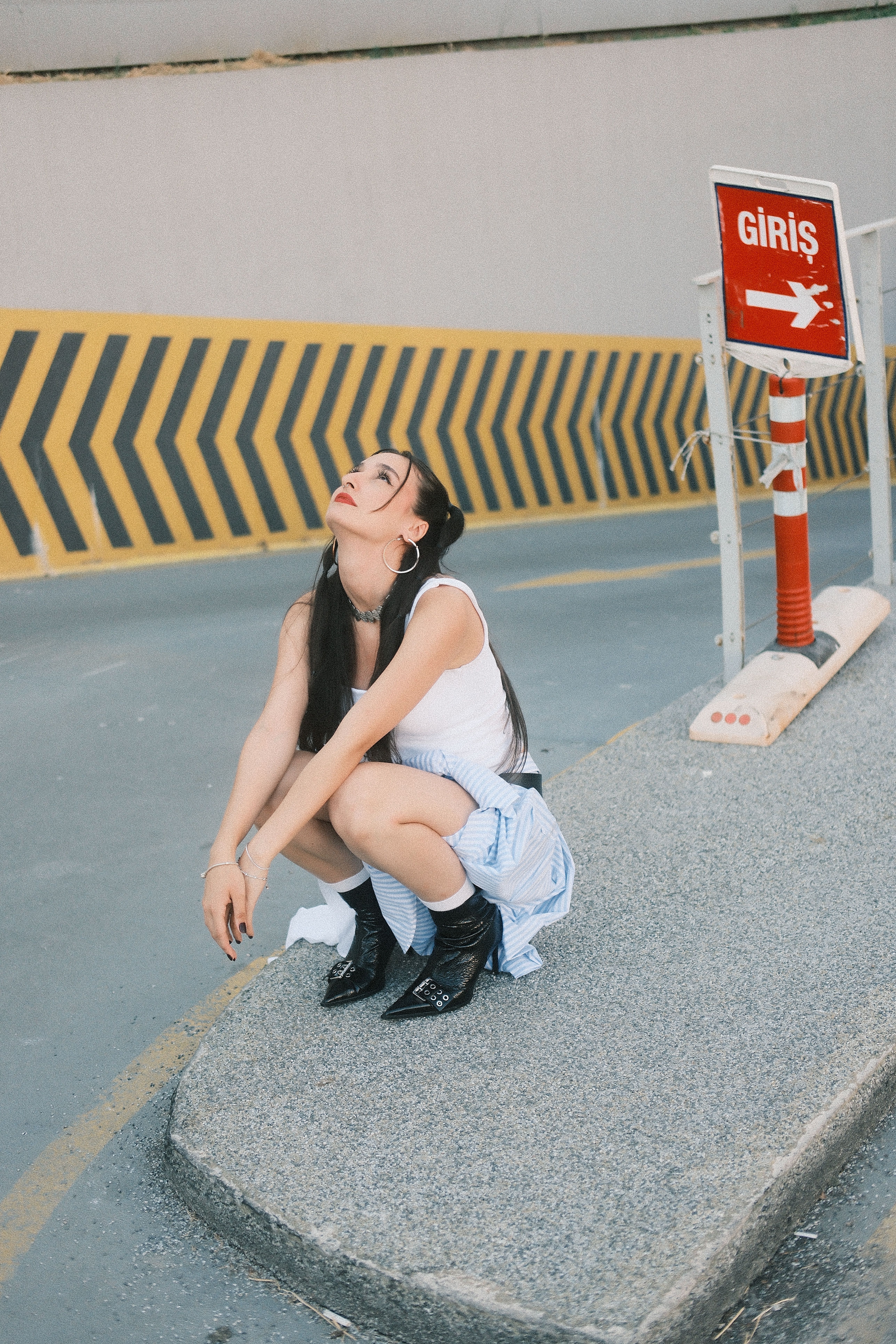 Woman crouching with playful expression beside warning sign in city