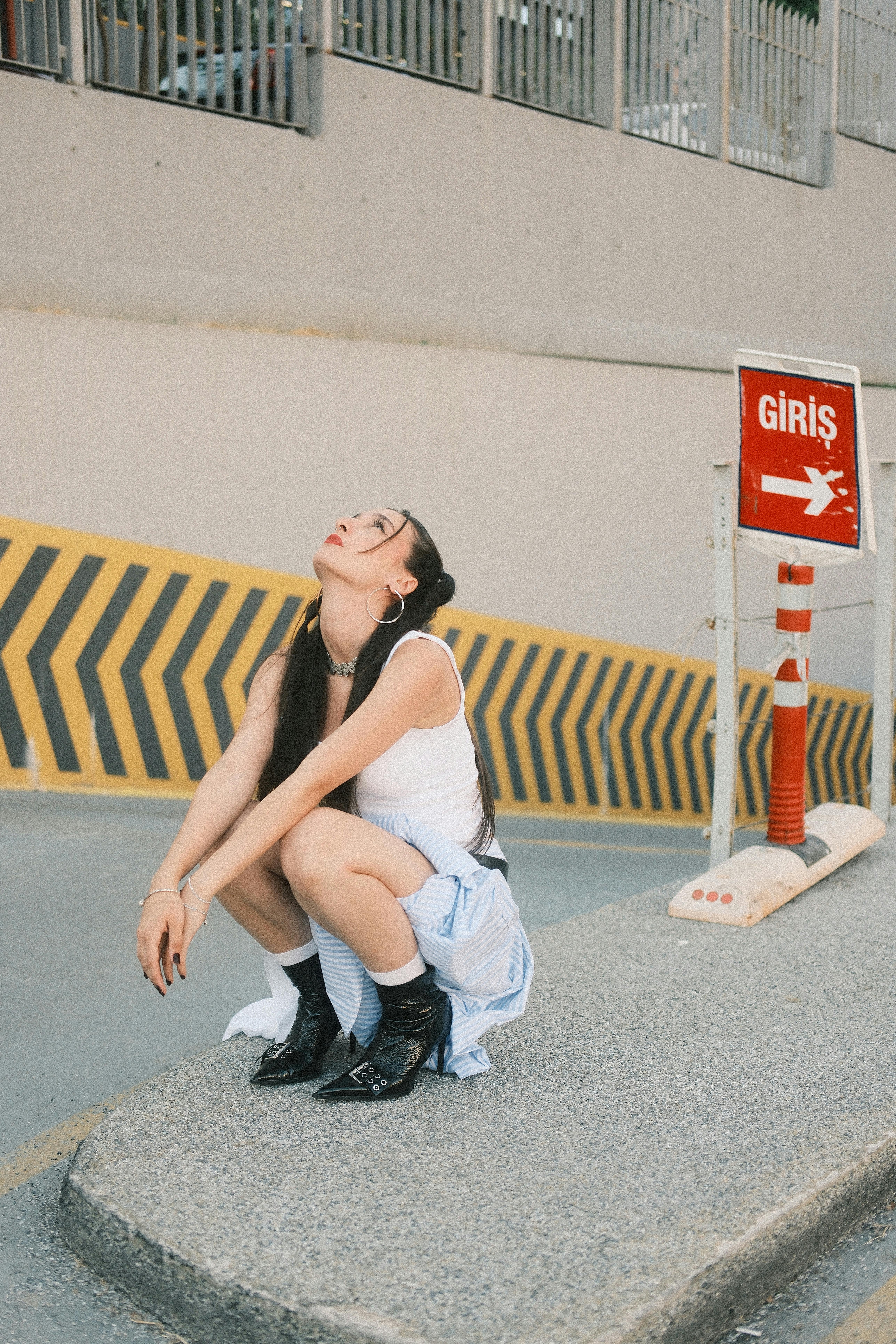 Young woman in urban setting squatting near a red entrance sign.