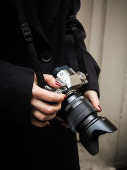 A person with red nails holding a DSLR camera, ready for photography.