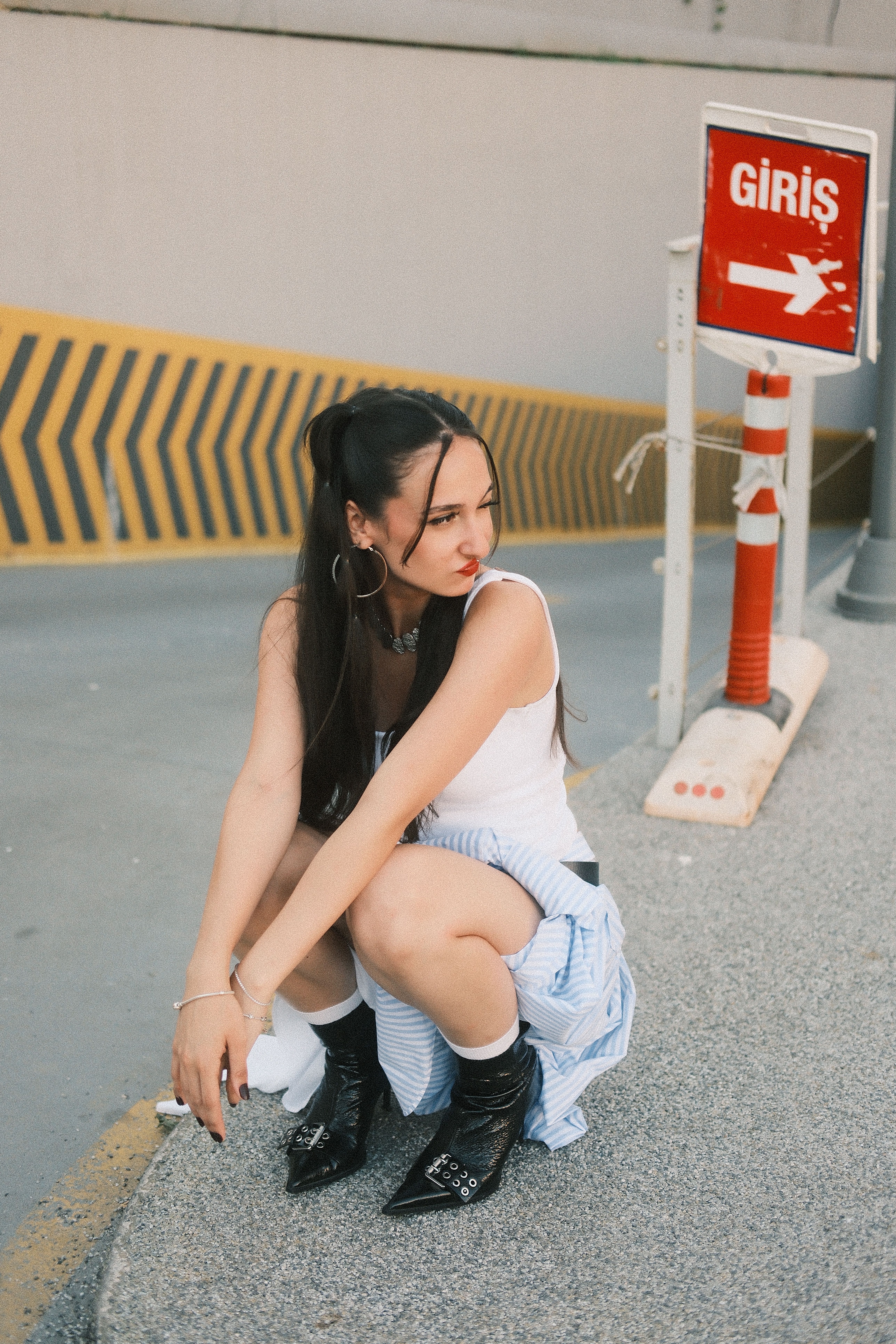 Stylish young woman squatting on urban street near a 'Giris' entrance sign, under daylight.