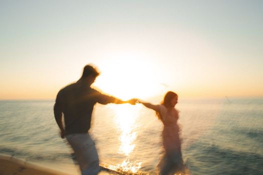 A blurred image of a couple holding hands while walking on the beach at sunset, evoking love and freedom.