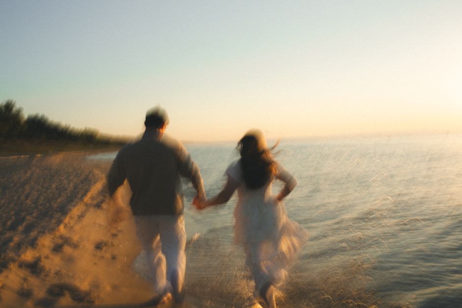 A blurred image of a couple running along a sandy beach at sunset, capturing motion and romance.