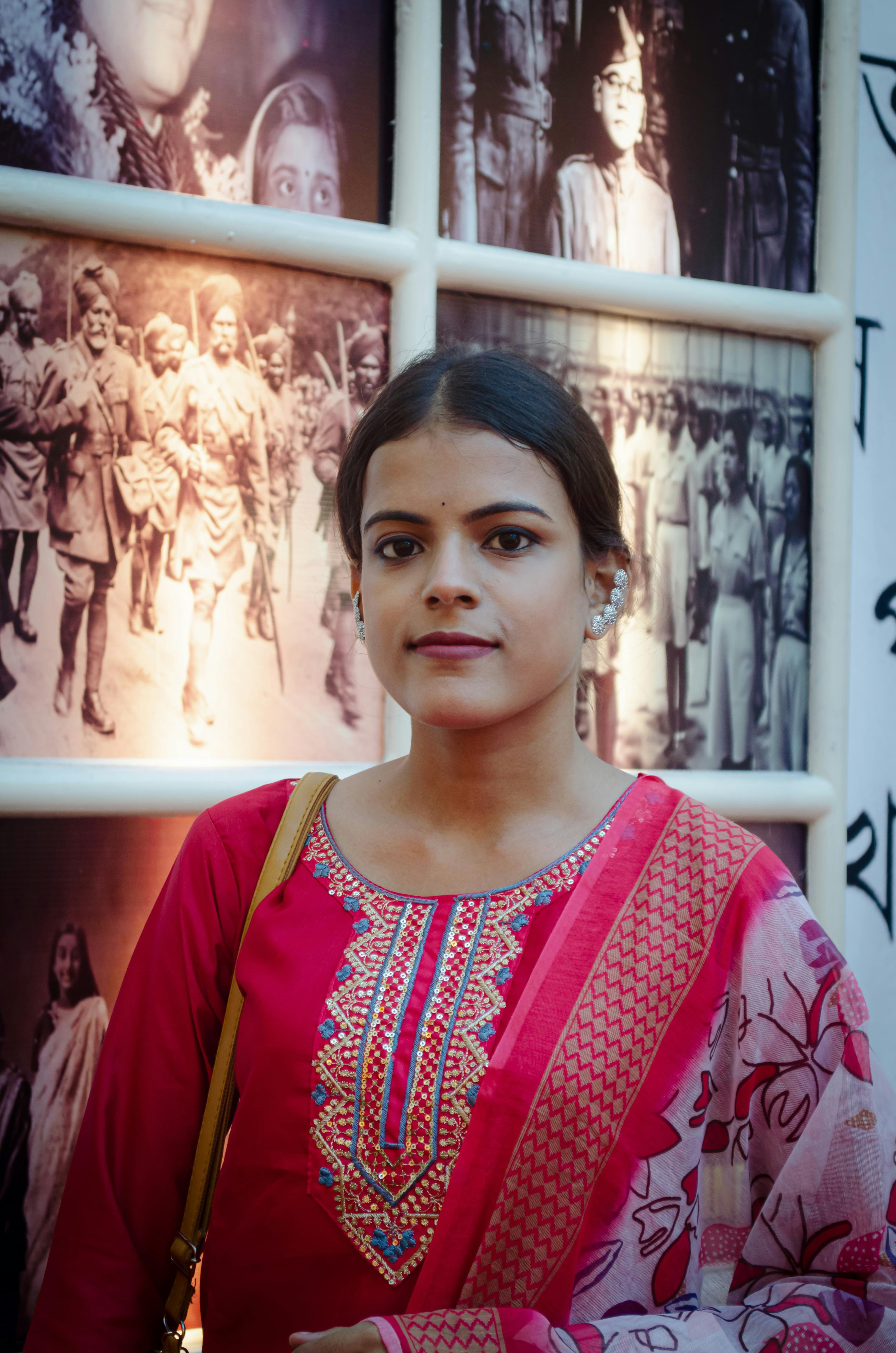 Young woman in traditional attire standing in front of a historical photo gallery, indoors.