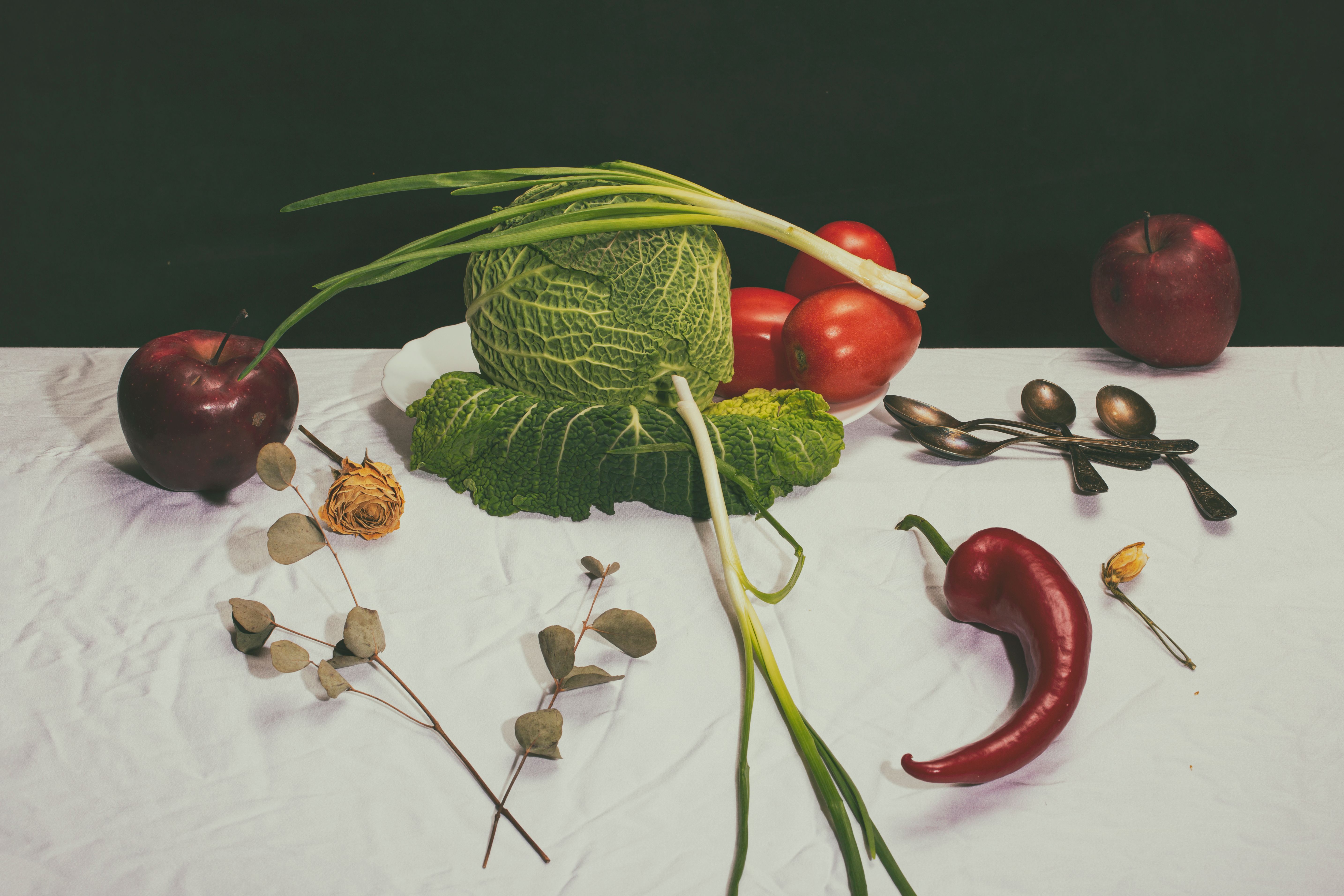 A vibrant still life of vegetables and fruits on a white tablecloth, featuring cabbage and apples.