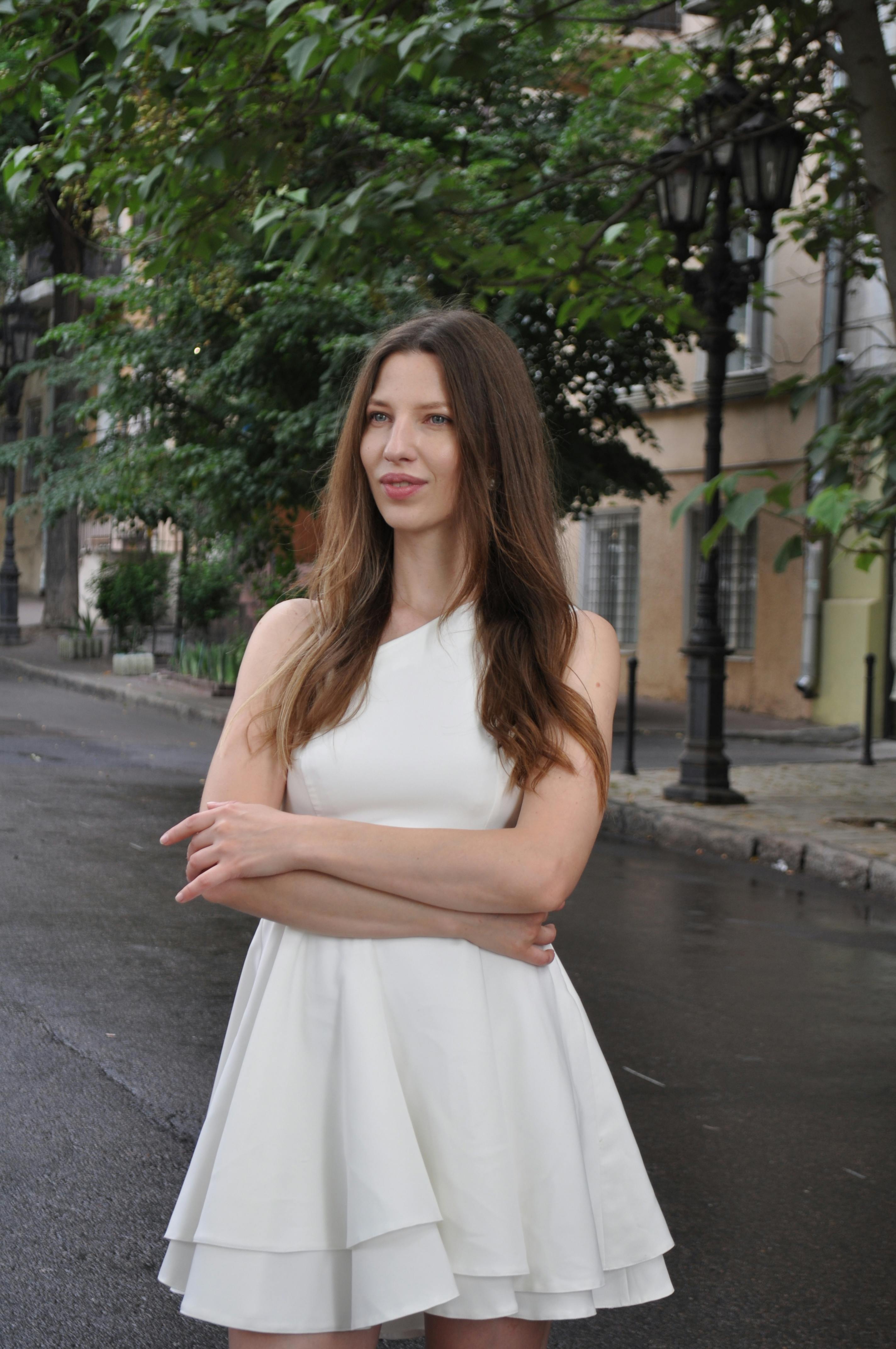 Elegant woman in white dress poses confidently outdoors in Odessa, Ukraine.