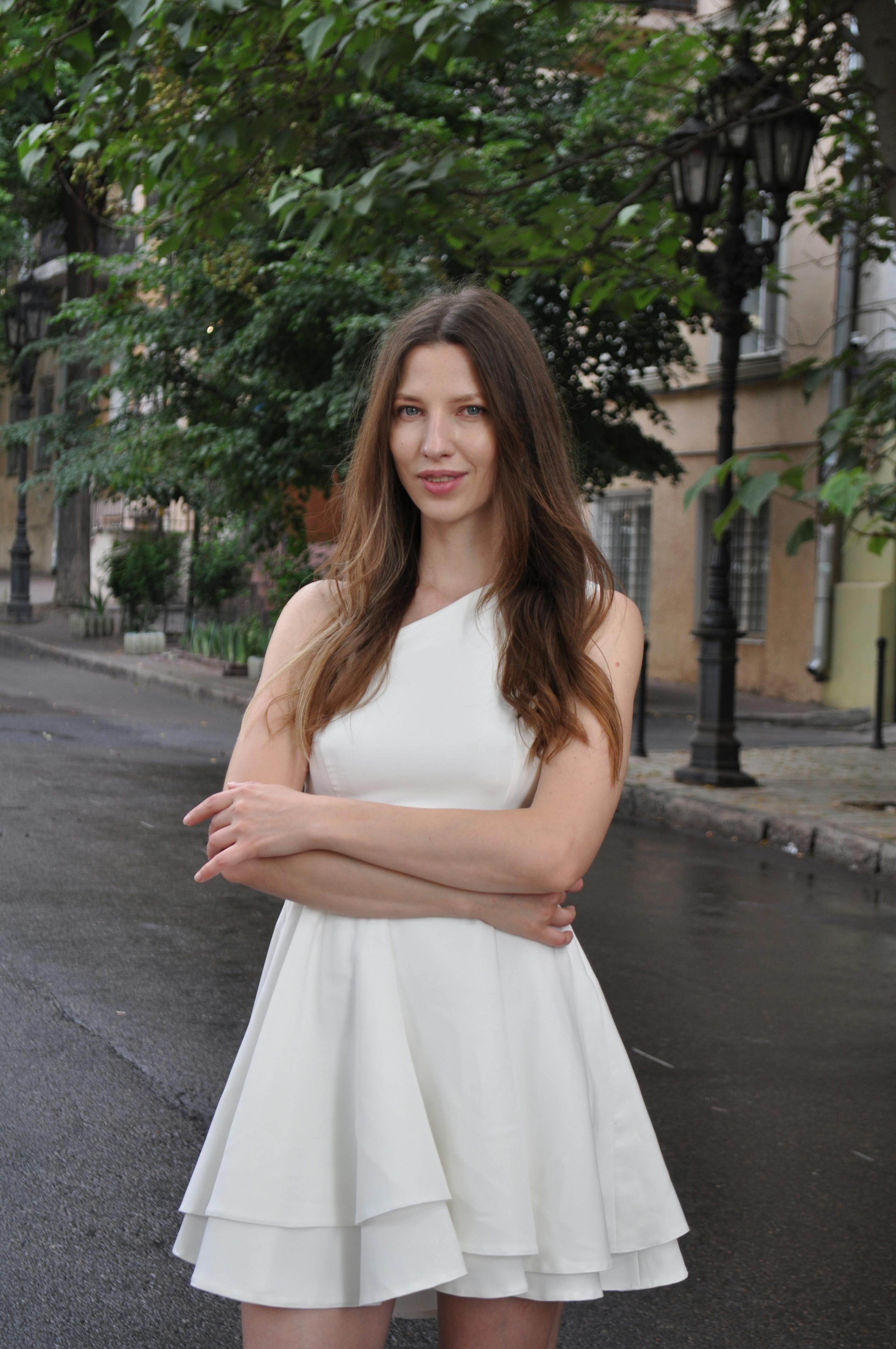 Elegant woman in a white dress posing on a quiet city street.