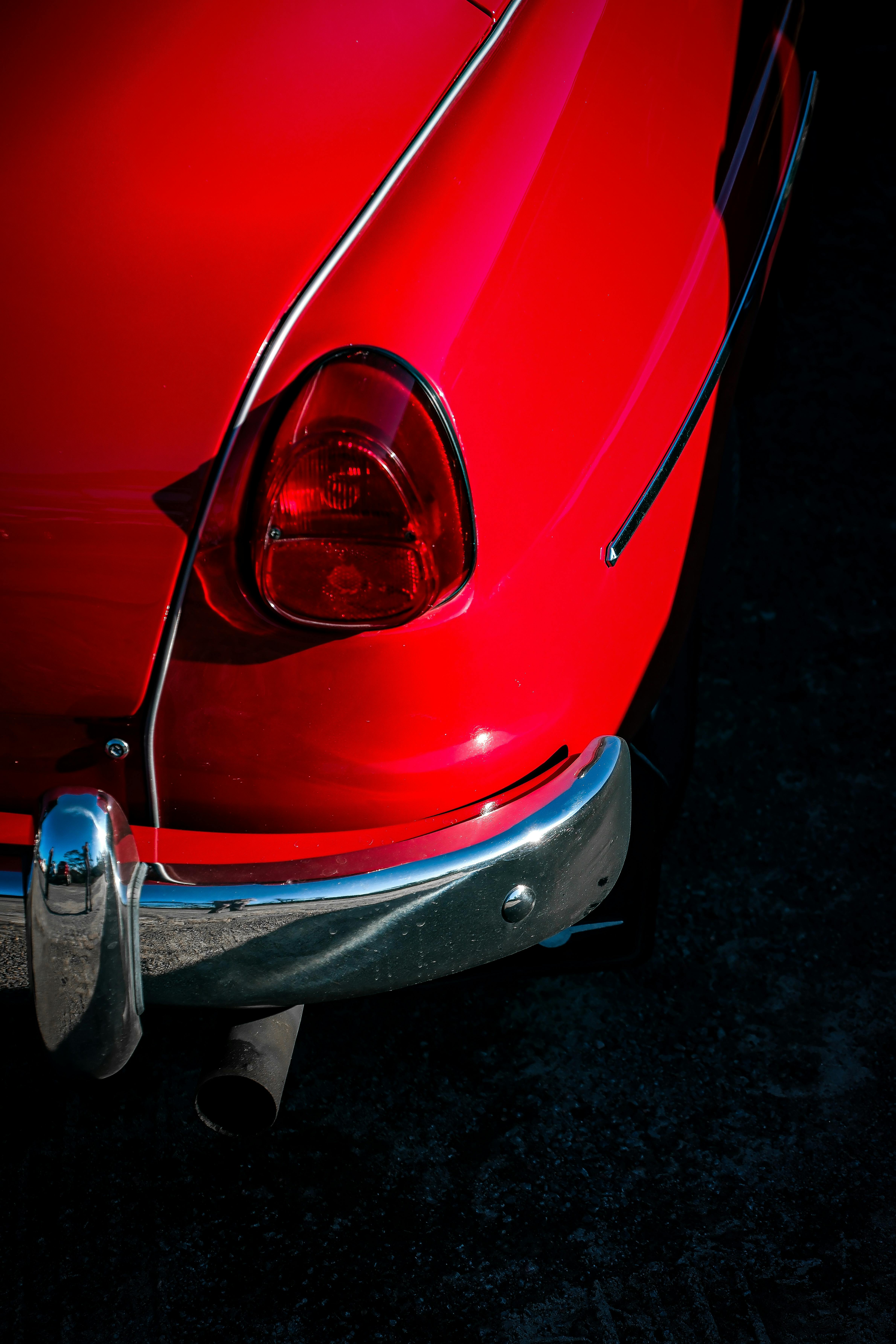Close-up of a classic red car's tail light and bumper, showcasing vintage automotive design.