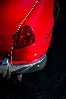 Close-up of a classic red car's tail light and bumper, showcasing vintage automotive design.