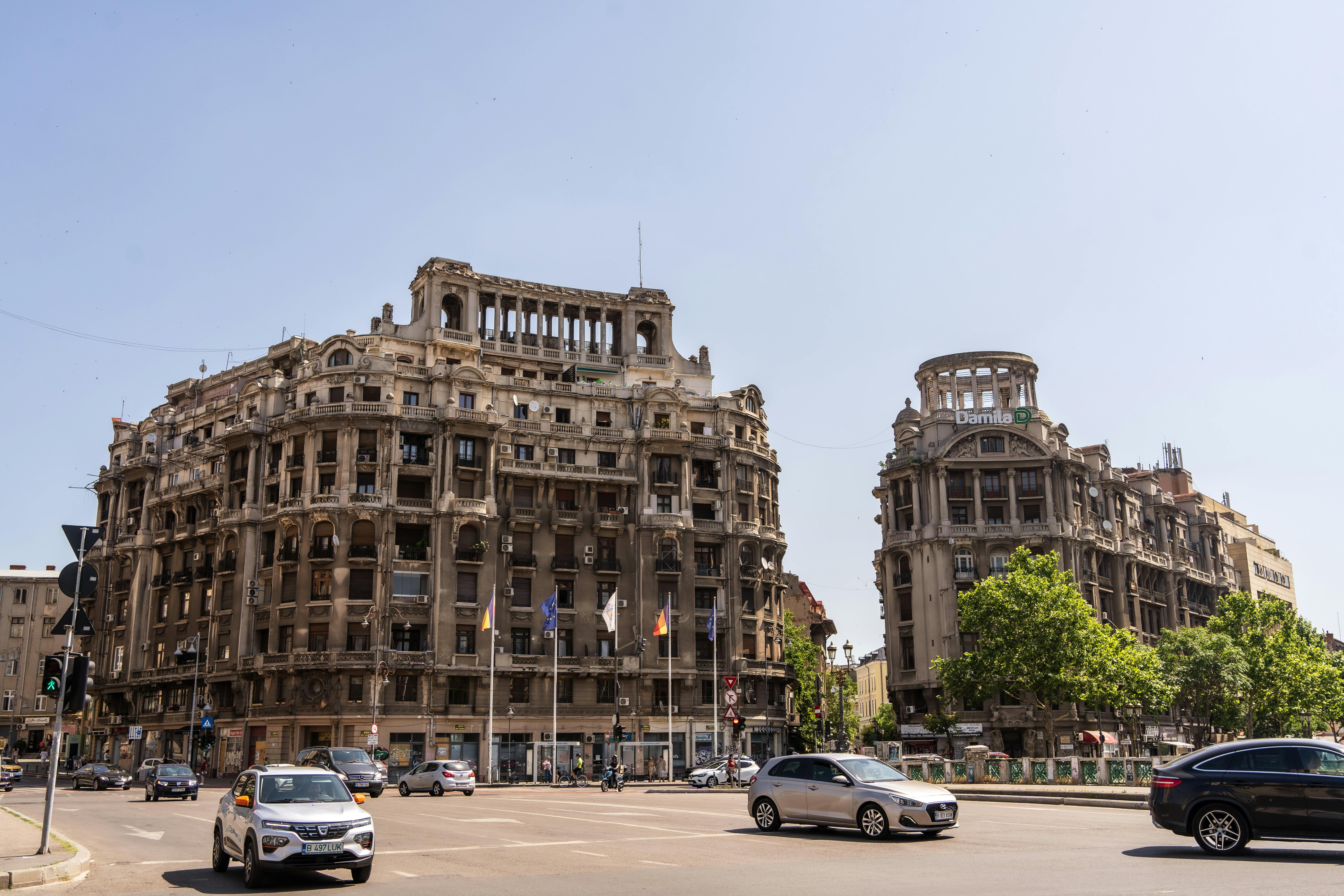 Großartige neoklassizistische Architektur in Bukarest, Rumänien, mit zwei historischen Gebäuden an einer belebten städtischen Kreuzung unter hellem Sommerhimmel.