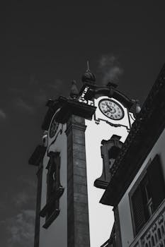 Monochrome image of a historical clock tower against the sky at daytime.