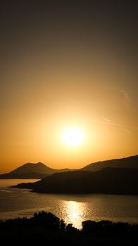 A picturesque sunset over calm waters and silhouetted hills, evoking serenity.