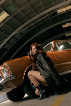 身着皮夹克的时尚女子倚靠在一辆经典汽车旁，身处室内环境中