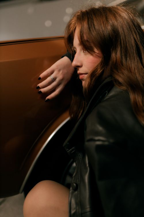 Free A thoughtful woman in a leather jacket sits near a car, reflecting mood. Stock Photo