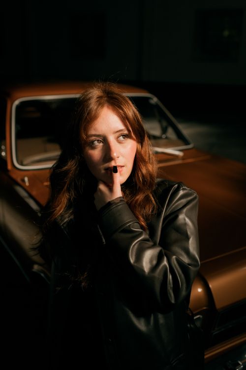 Free A thoughtful young woman in a leather jacket stands by a vintage car. Stock Photo