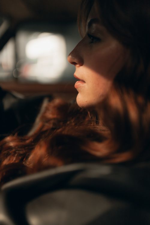 Free Side profile of a woman in a car, immersed in shadows with warm lighting. Stock Photo