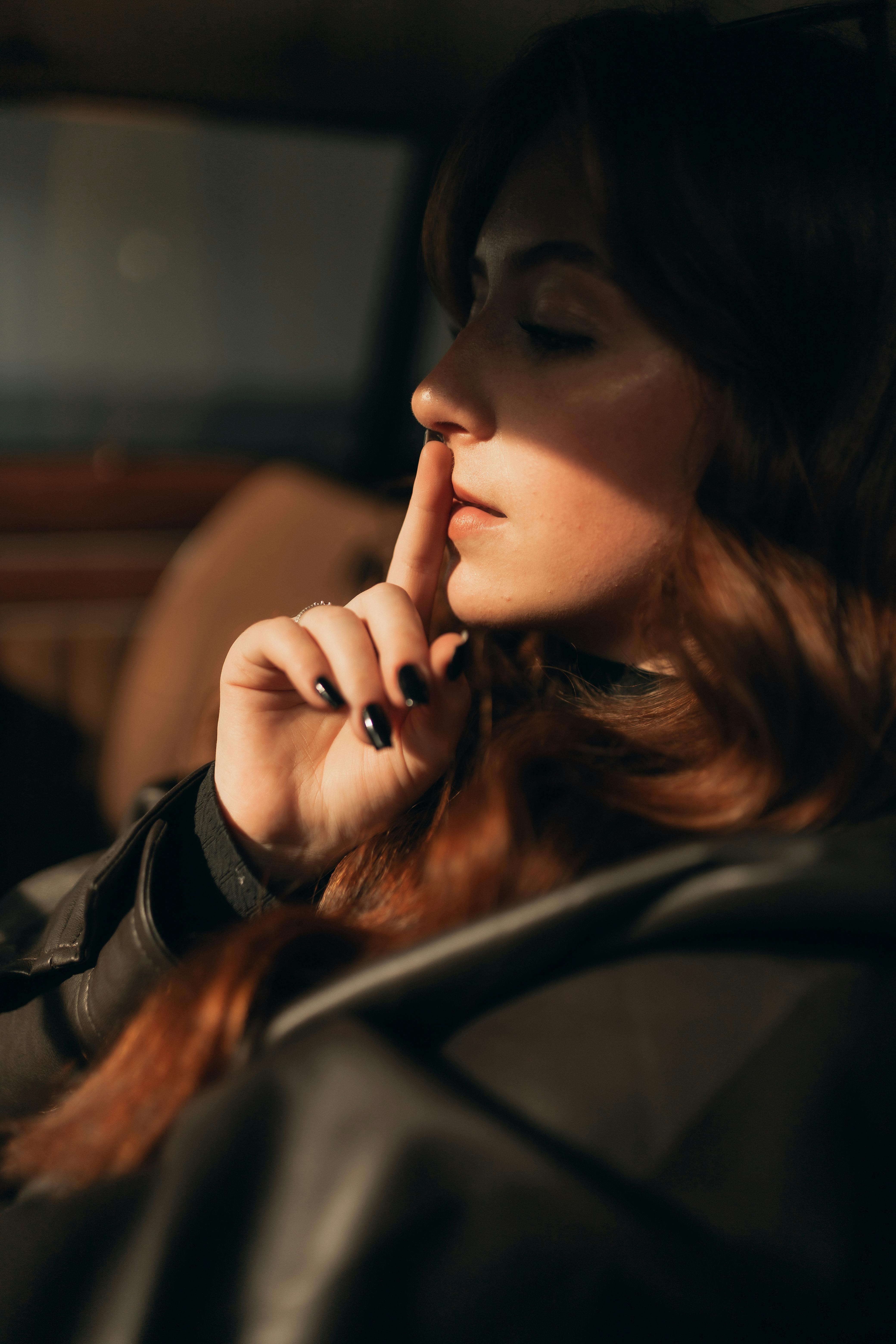 Young woman in dimly lit car interior with thoughtful expression and dramatic lighting.
