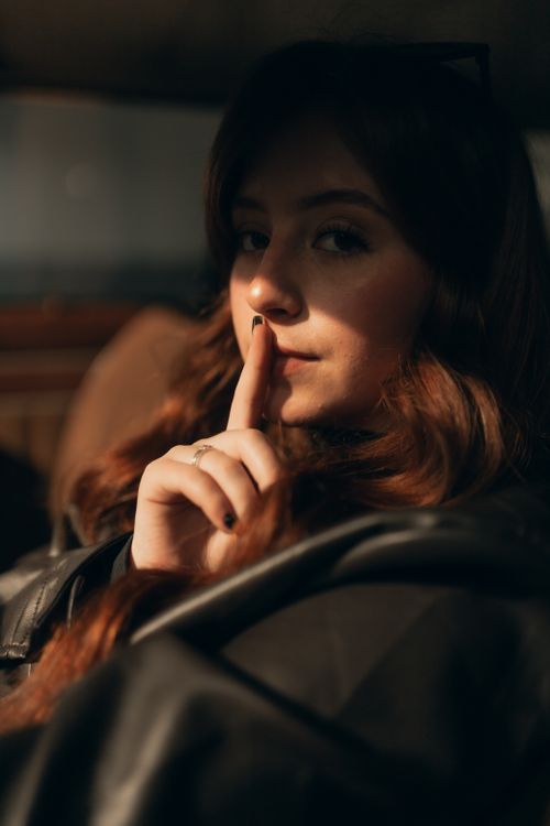 Free A young woman with long hair gestures silence, creating a mysterious atmosphere. Stock Photo