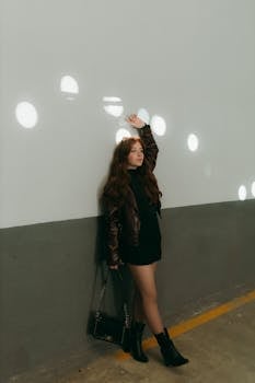 Fashionable woman poses against a wall with light spots indoors.
