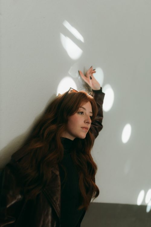 Free Artistic portrait of an adult woman in a brown jacket with sunlight reflections on a wall. Stock Photo